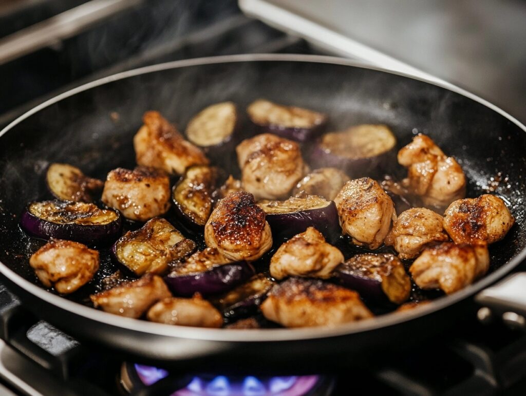 Chicken and eggplant cooking in a skillet with steam rising on a stovetop