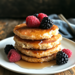 A stack of golden-brown keto cottage cheese pancakes with berries and syrup